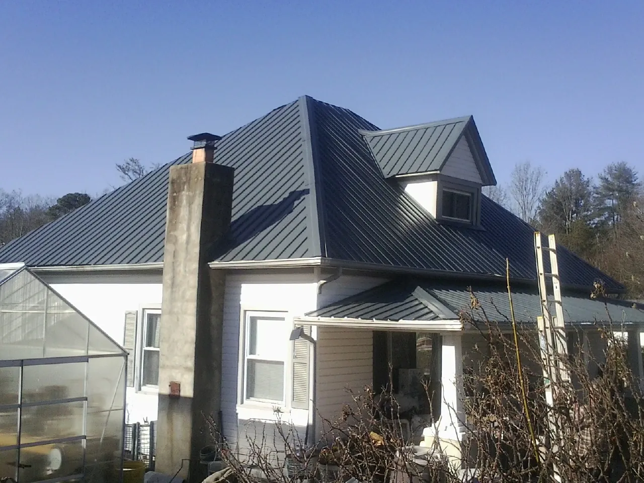 Dark blue standing seam metal roof on a white farmhouse with dormer — Slate & Tile Roof Repair by Roofing Brothers in Harbor City