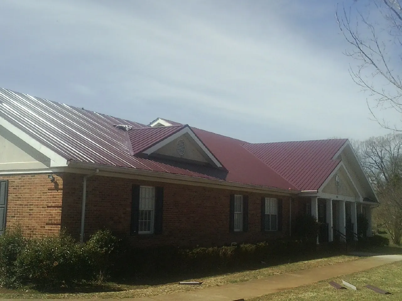 Red metal roof with gabled entries on a long brick building, from a Hail Damage Roof Repair job in Harbor City