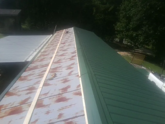 Old rusted panels beside newly installed green metal roofing — Wind Damage Roof Repair by Roofing Brothers in Harbor City