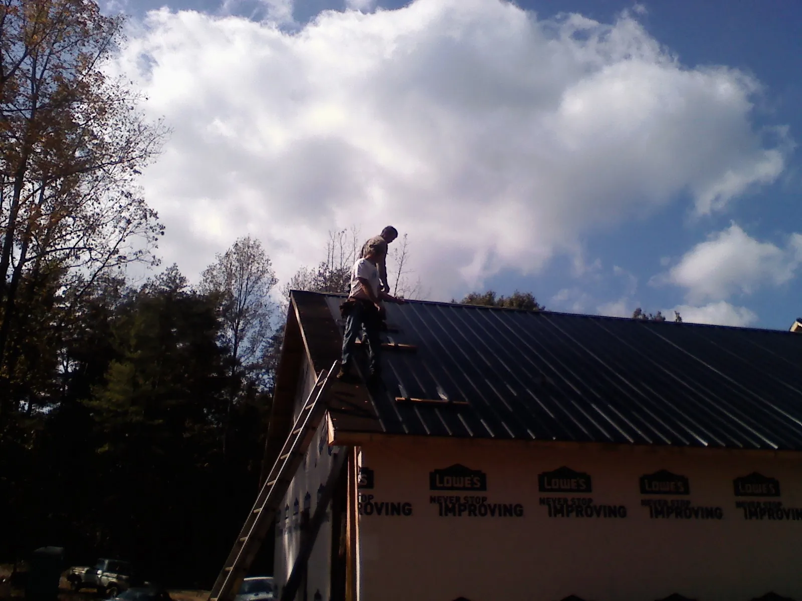 Roofer fastening dark metal panels high against a cloudy sky, from a Roof Inspection job in Harbor City